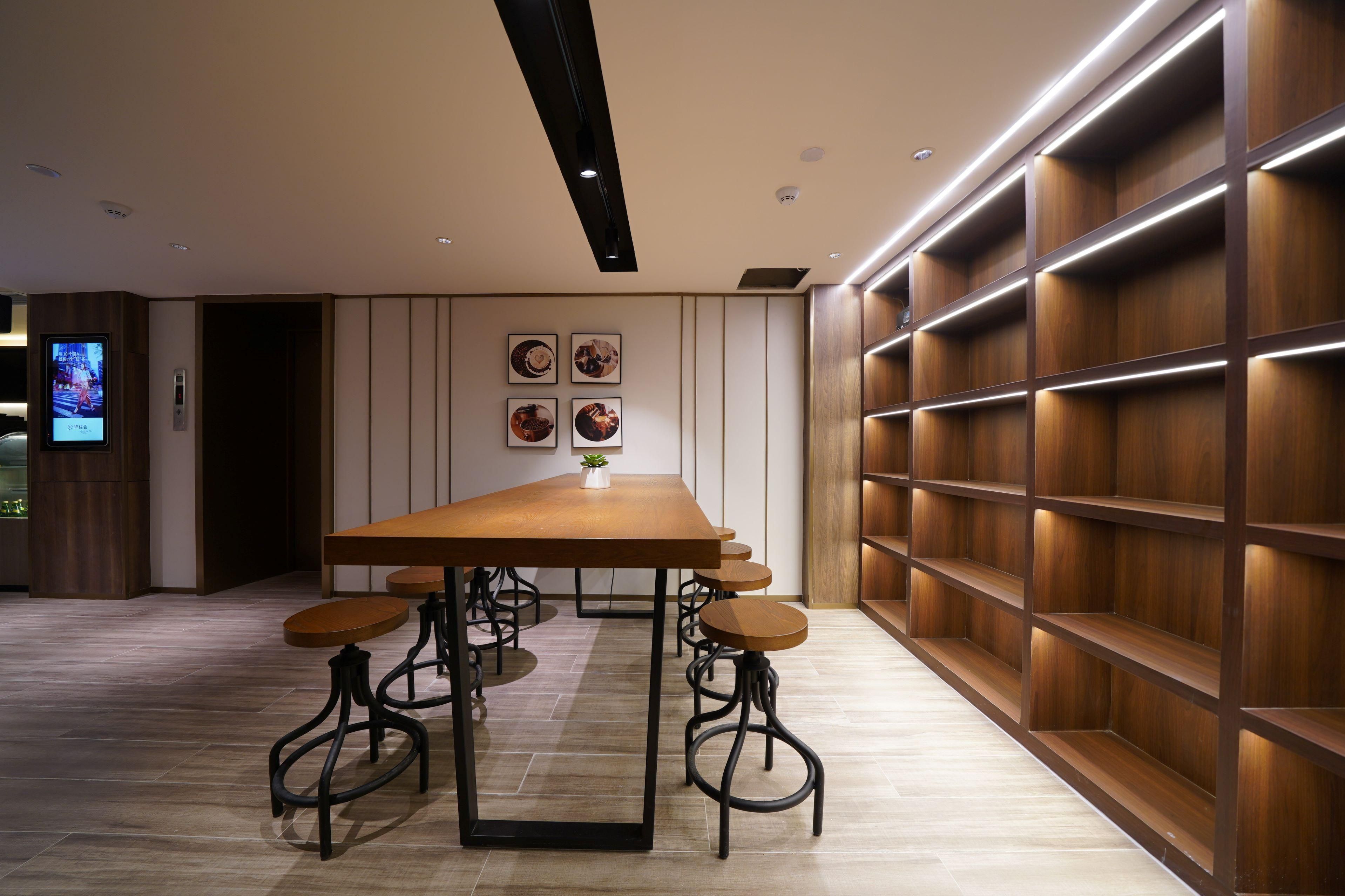 Un interior moderno con una mesa de madera, taburetes de bar, iluminación empotrada y un estante montado en la pared.