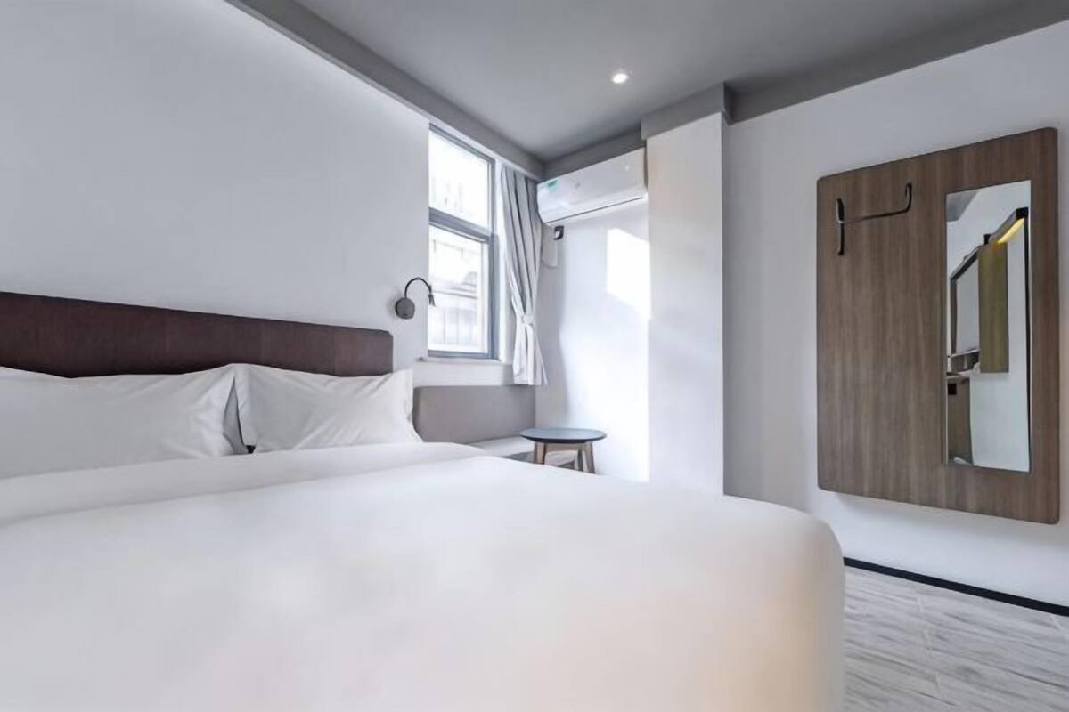 A modern hotel room with a large bed, a small round table, a wardrobe, and a window with curtains.