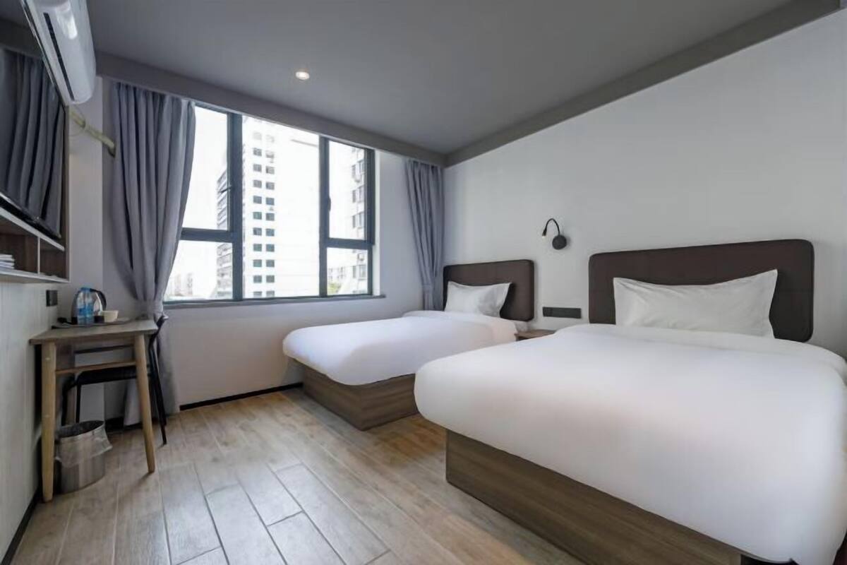A hotel room with two beds, a desk, a chair, a small table, and a window with curtains.