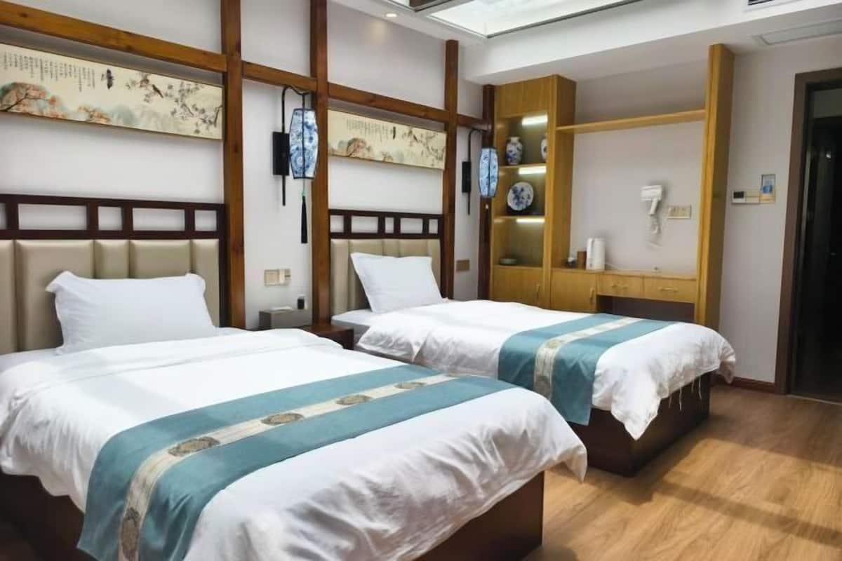 Ein Hotelzimmer mit zwei Betten, Holz-Kopfteilen, einem an der Wand befestigten Regal mit Dekoration und einem Oberlicht.