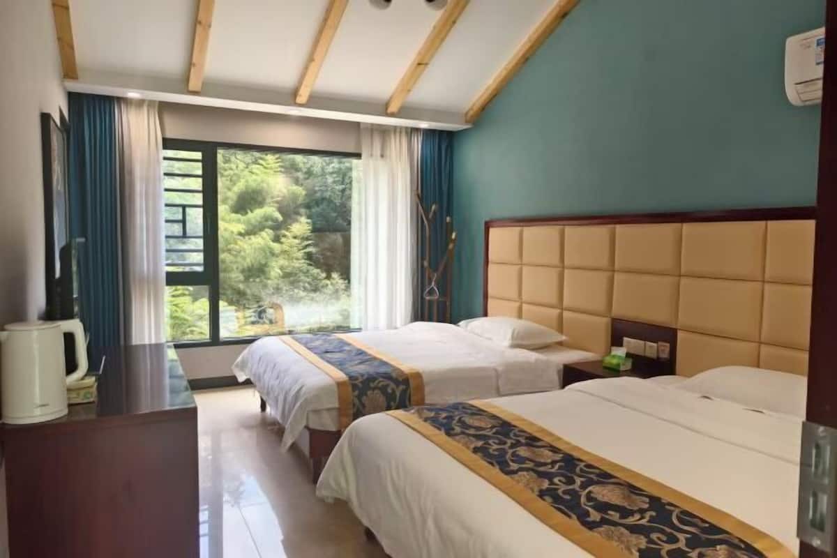 Ein Hotelzimmer mit zwei Betten, einer Holzbalkendecke, Blick auf Grünflächen und einem Fenster mit Vorhängen.