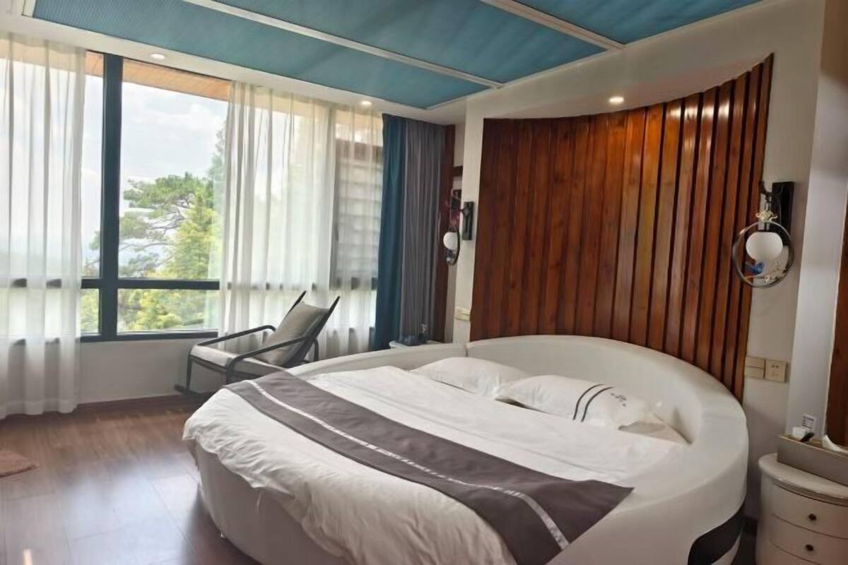 Ein modernes Hotelzimmer mit einem großen Bett, einer Wand mit Holzvertäfelung, einem Fenster mit Vorhängen und einem Sessel.