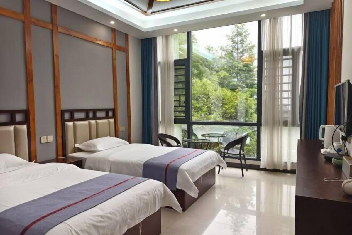 Ein Hotelzimmer mit zwei Betten, einem Schreibtisch und einem großen Fenster mit Blick ins Grüne.