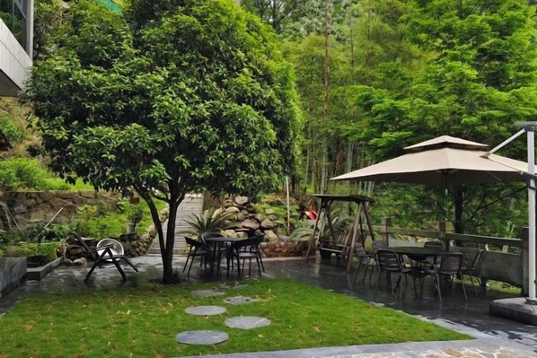 Un patio con mobiliario exterior, un árbol y un área cubierta.