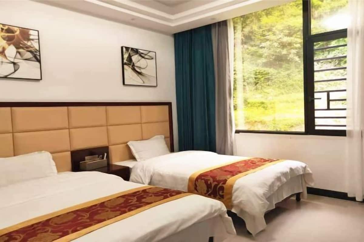 Ein Hotelzimmer mit zwei Betten, einem Kopfteil, einem Fenster mit Vorhängen und Bildern an der Wand.