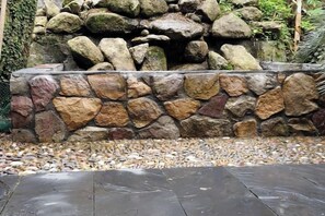 Un muro de piedra con rocas de distintos tamaños y una terraza de madera al frente.