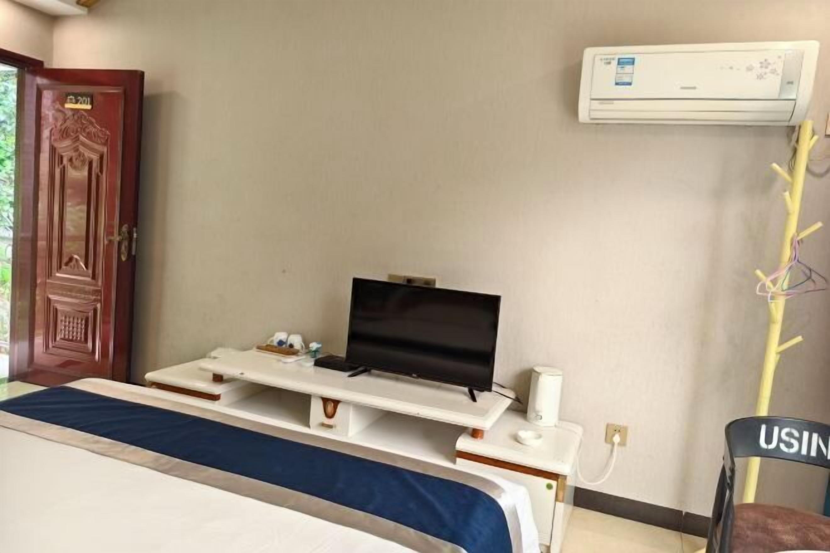 Una camera d'albergo con un letto, una televisione, una scrivania con un computer, un condizionatore d'aria e una sedia.