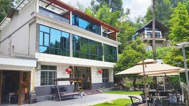A modern two-story building with large windows, a patio area with outdoor seating, and a lush green garden. - Mingjing Mountain House on the halfway of Hengshan Mountain (Hengyang)