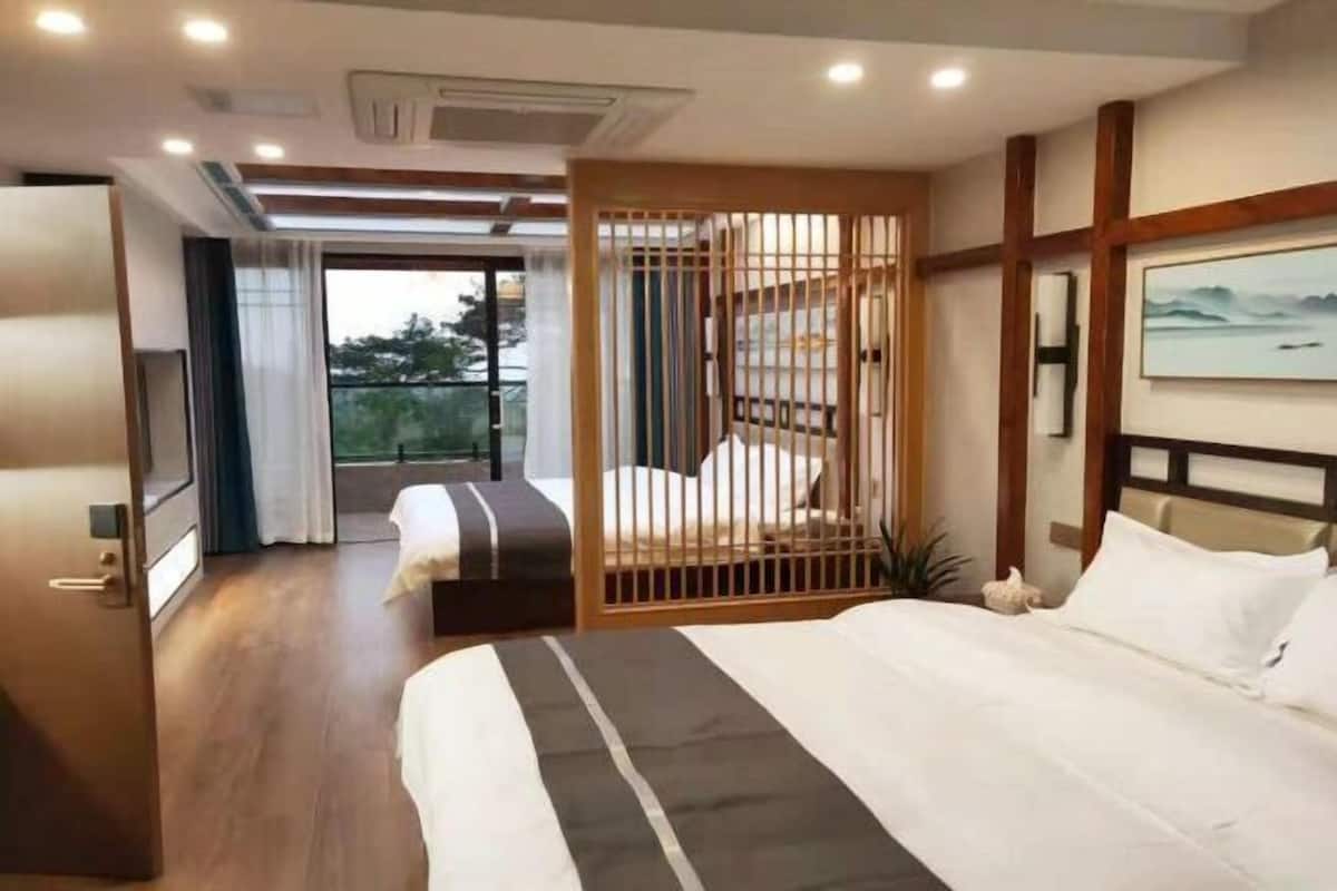 Ein Hotelzimmer mit einem großen Bett, einem kleineren Bett, einer Holzwand, einem Balkon und einem Bild an der Wand.