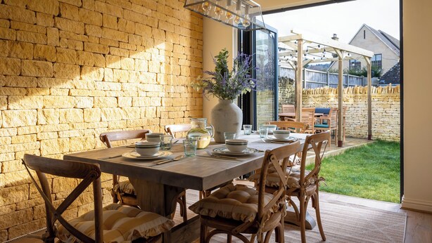 A dining area with a brick wall, wooden furniture, and a view of the backyard. - Broadway Country Chic Cottage (Broadway)