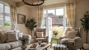 A cozy living room with a sofa, armchair, and ottoman, a wooden coffee table, and a view of the outside. - Broadway Country Chic Cottage (Broadway)
