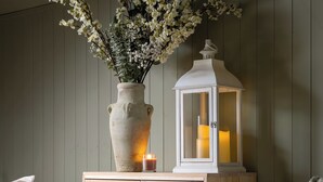 A bedroom with a wooden cabinet, a vase with flowers, and a lit lantern. - Broadway Country Chic Cottage (Broadway)