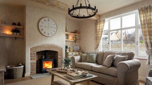 A cozy living room with a fireplace, a sofa, a coffee table, and a large wall clock. - Broadway Country Chic Cottage (Broadway)