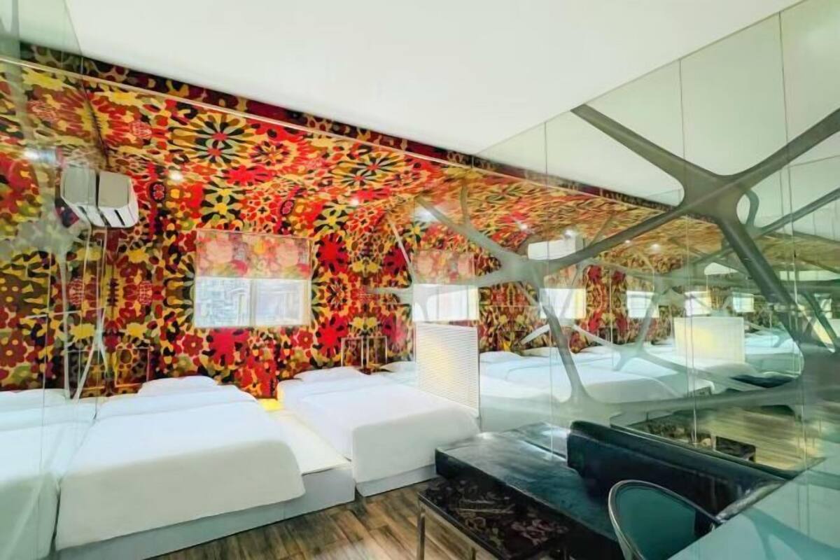 A modern hotel room with a vibrant floral wall design, a glass partition, and a comfortable seating area.