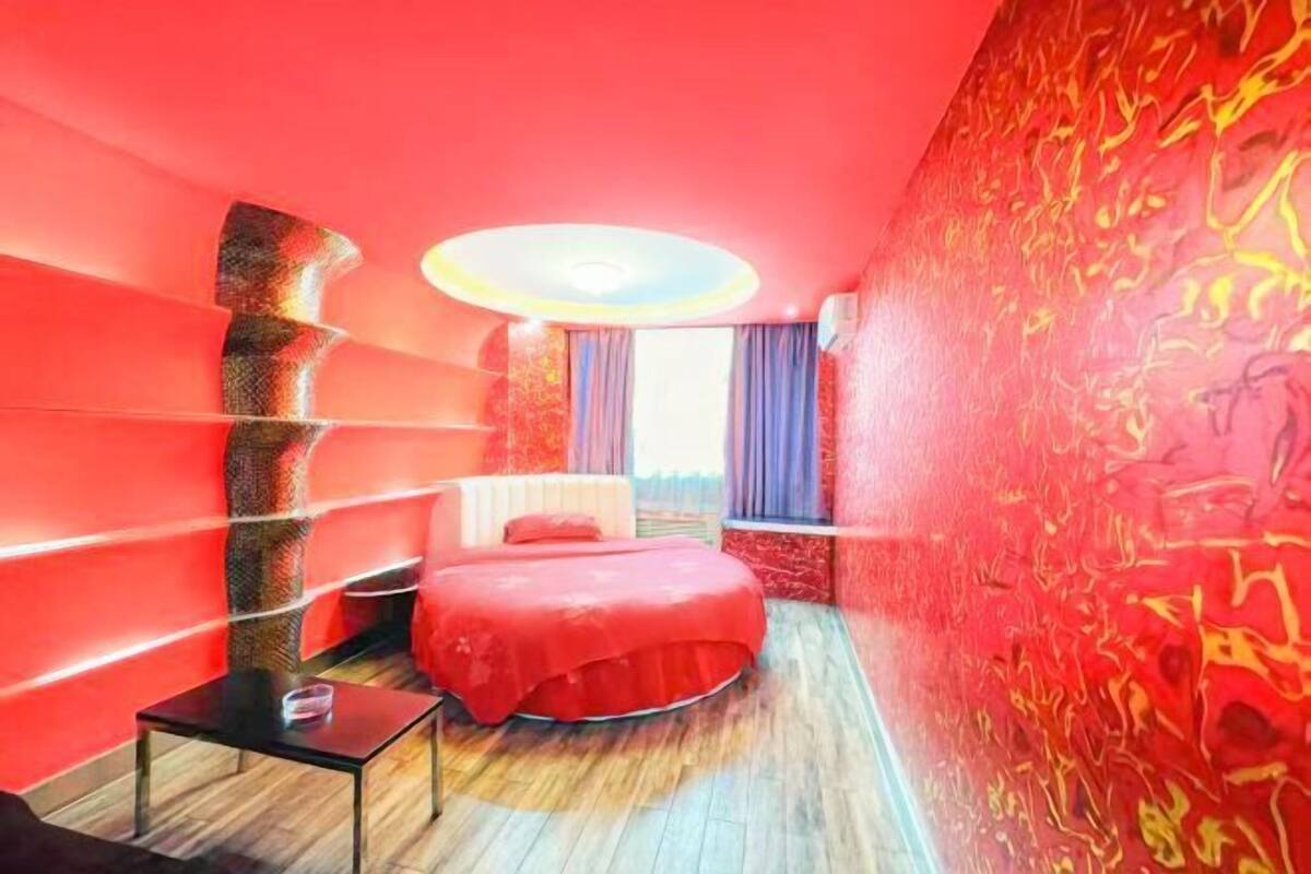 A room with a red bed, a small table, and a unique wall design.