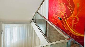 Una escalera con barandillas de vidrio, una pared roja con diseños abstractos y una cortina blanca.