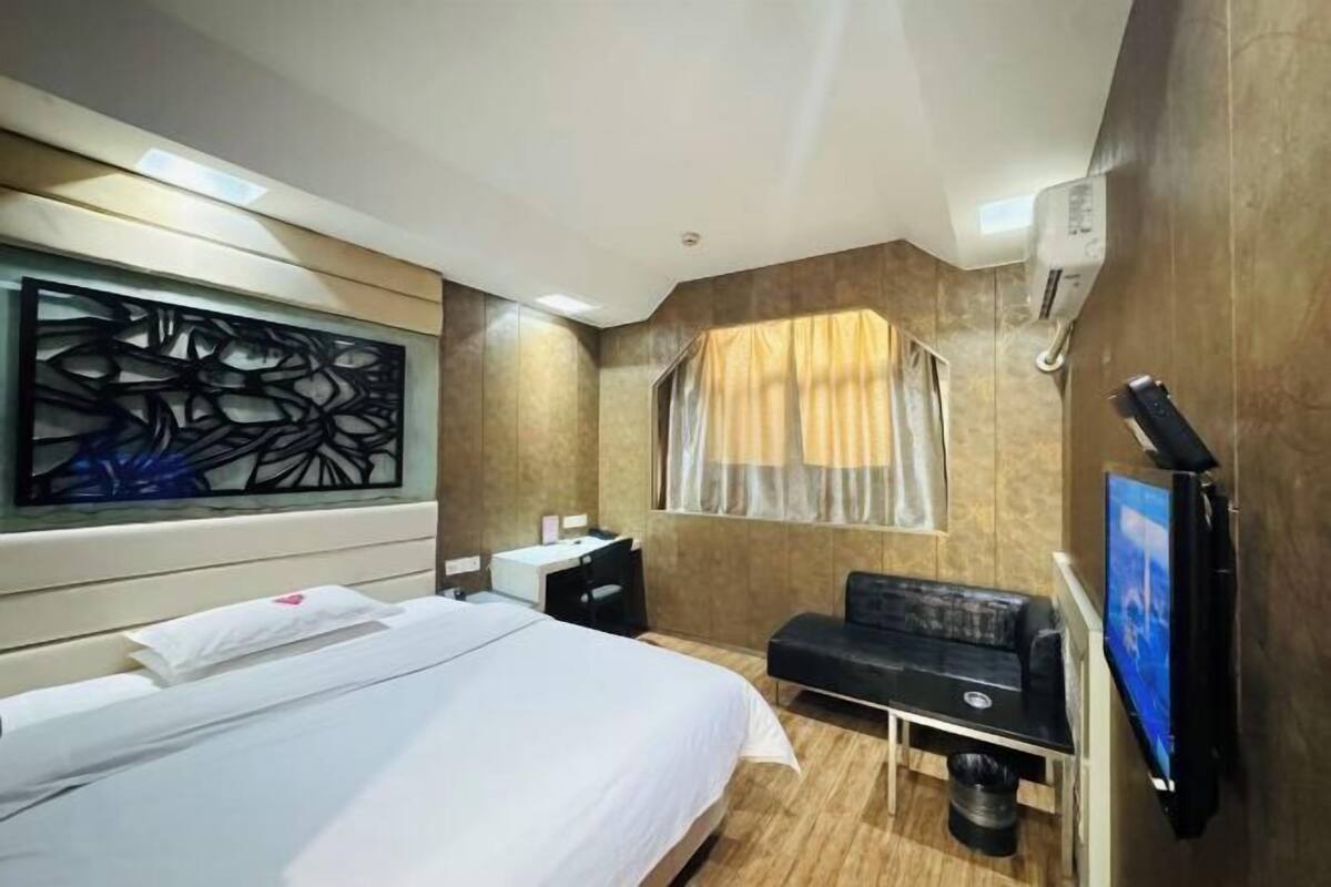 A hotel room with a bed, a desk, a chair, a TV, and a window with curtains.
