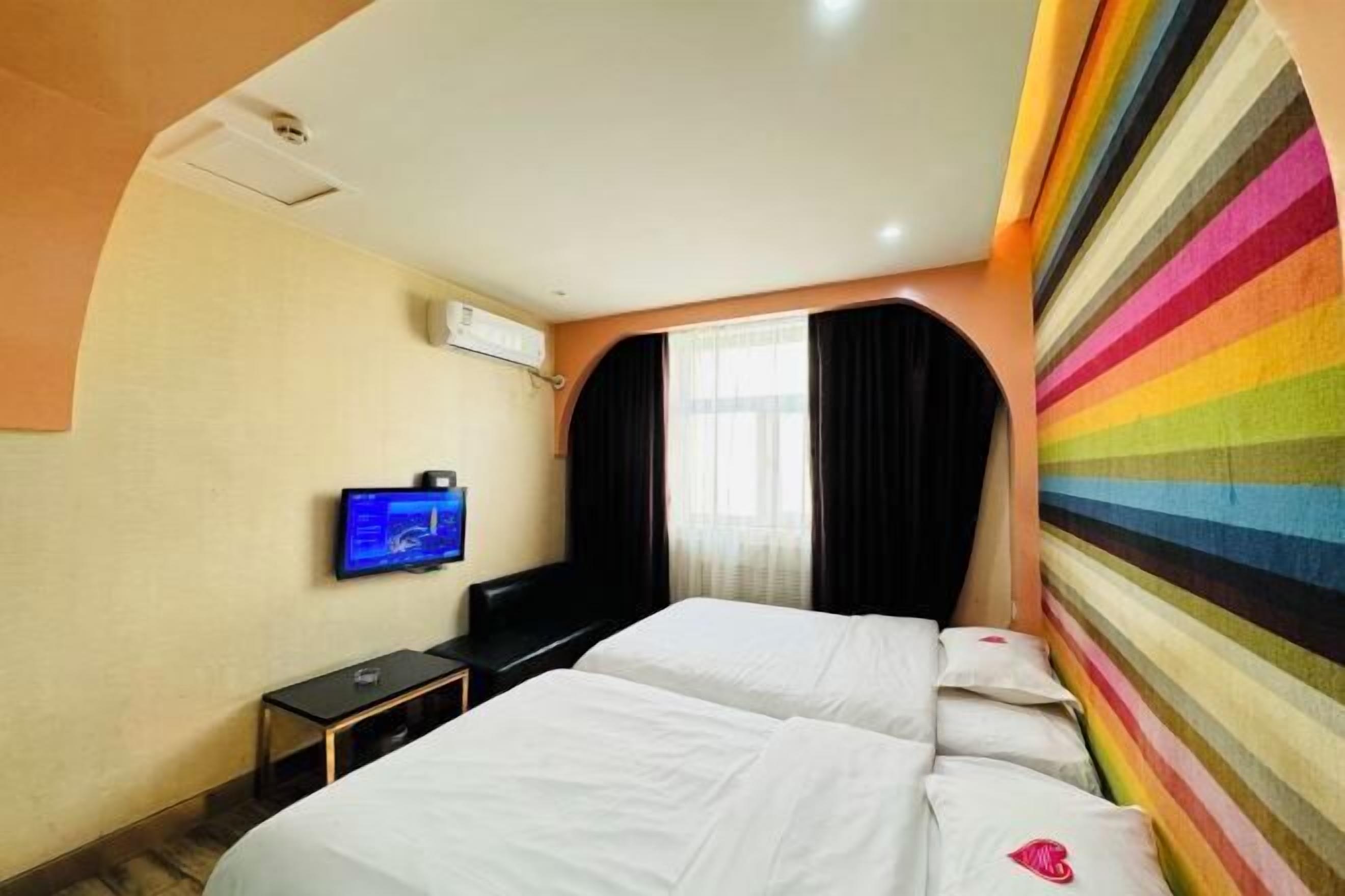 A hotel room with two beds, a flat-screen TV, a small table, and a window with curtains.