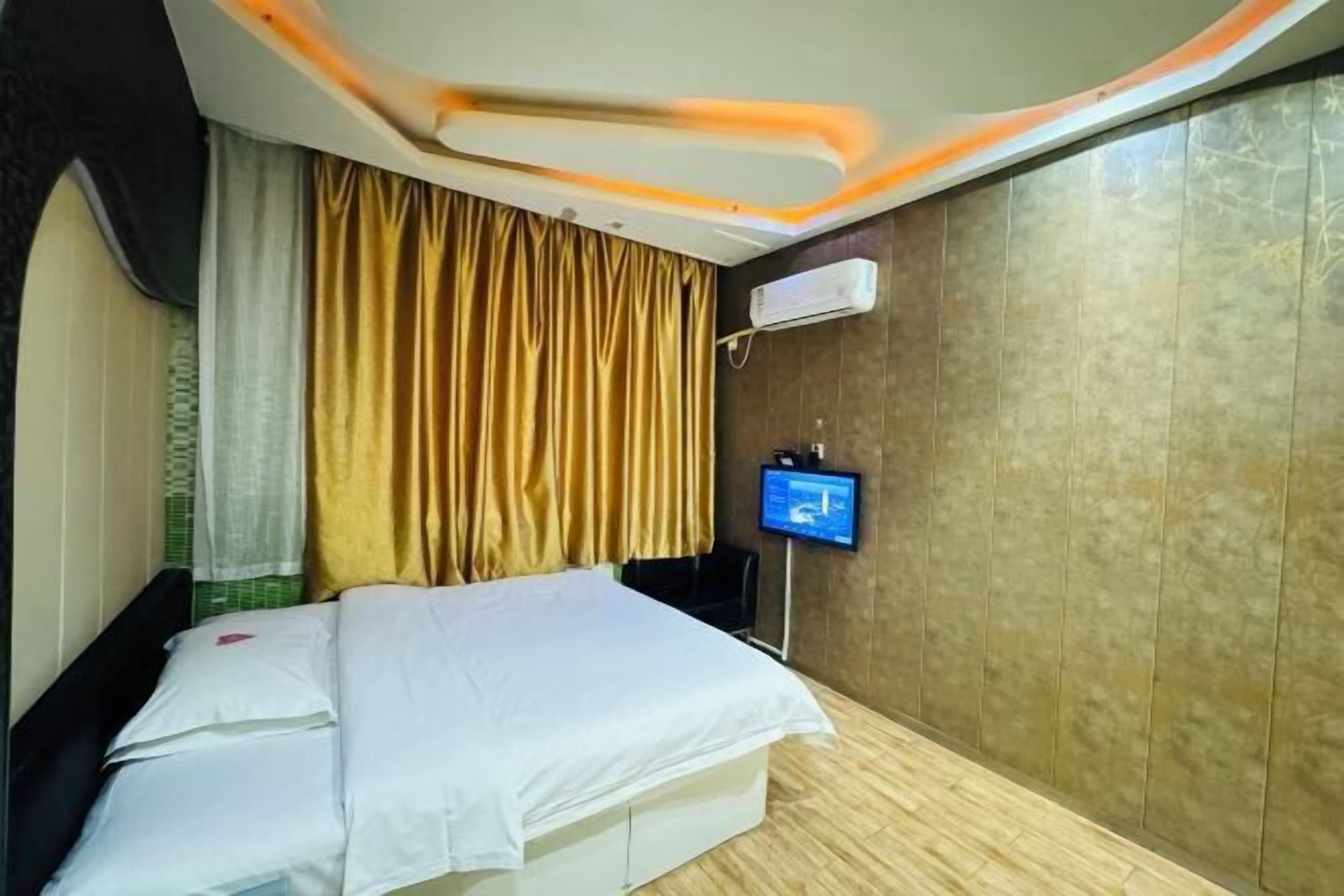 Una habitación de hotel con cama, cortinas, televisor y aire acondicionado.