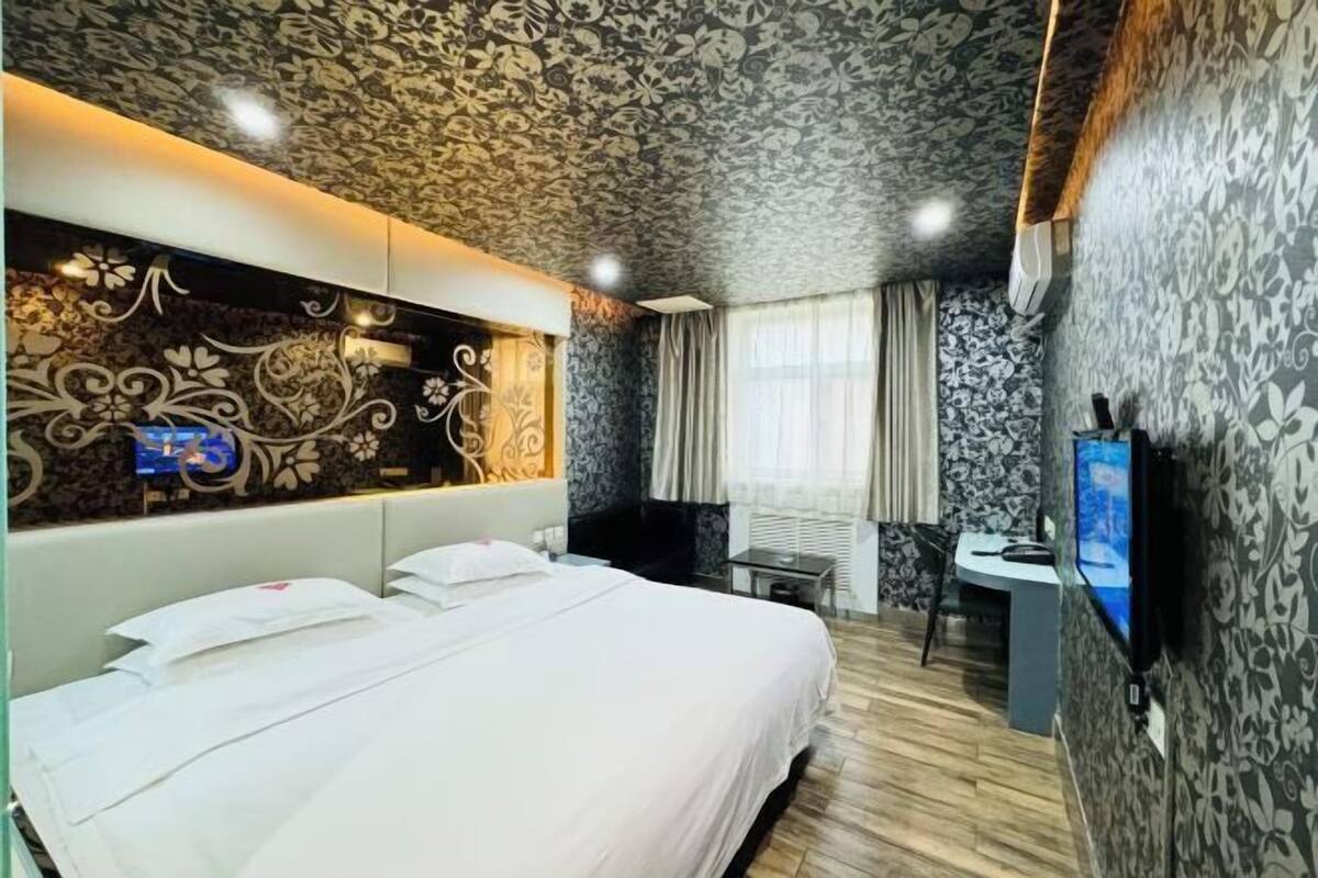 A hotel room with a large bed, a desk with a chair, a television, and a decorative wall panel.
