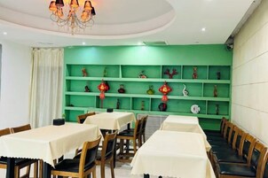 Un comedor con mesas y sillas, una pared verde con estantes y una araña.