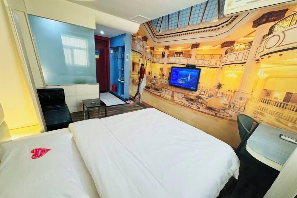 A hotel room with a bed, a TV, a desk, and a balcony with a view of the city.