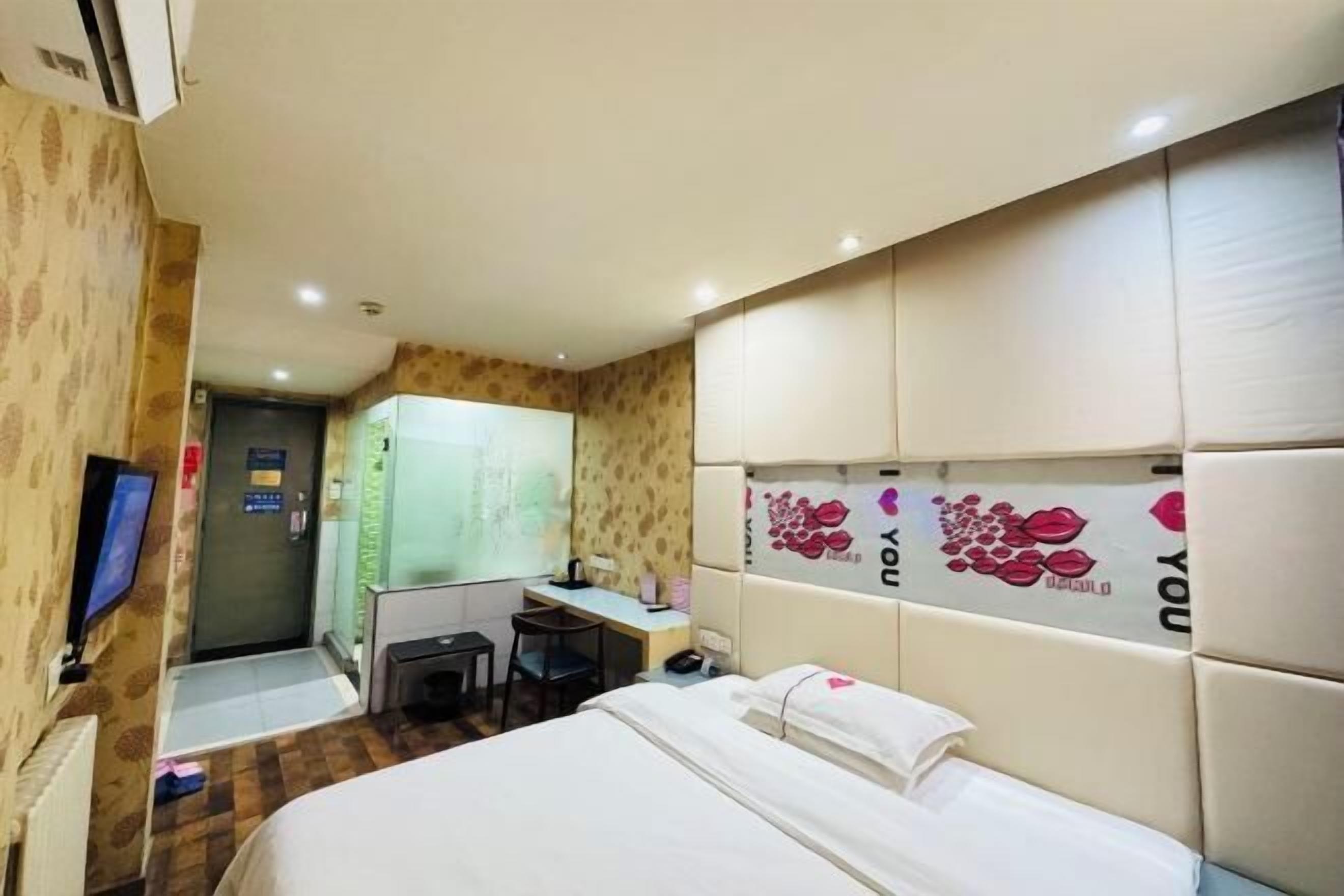 Quarto de hotel com uma cama, uma escrivaninha, uma cadeira e uma televisão.