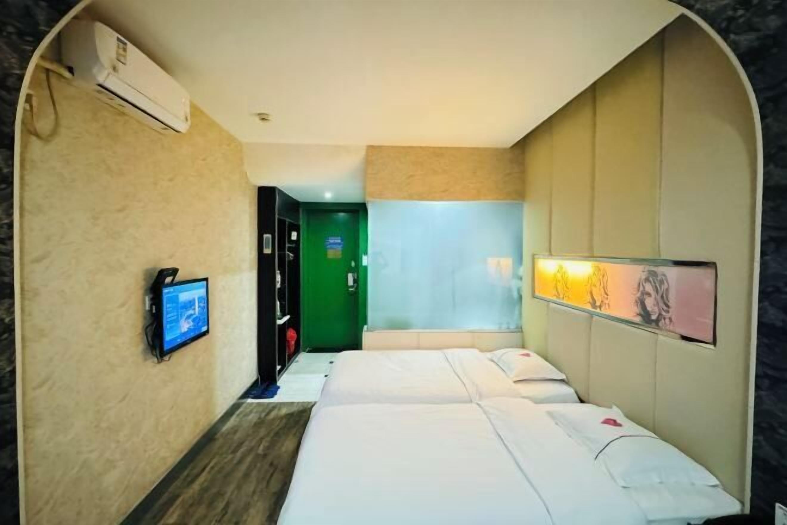 A hotel room with two beds, a TV, a green door, and a wall-mounted air conditioner.
