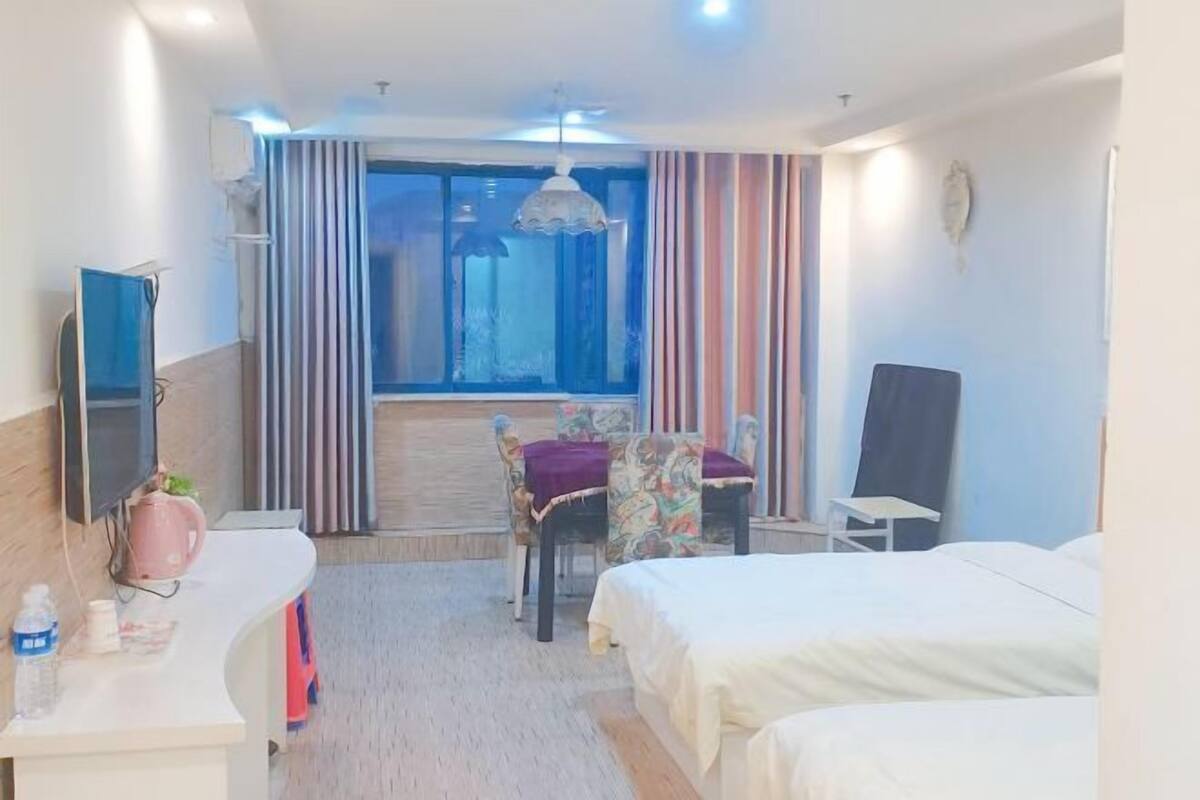 Habitación de hotel con cama, escritorio con computadora, silla, ventana con cortinas y televisor.