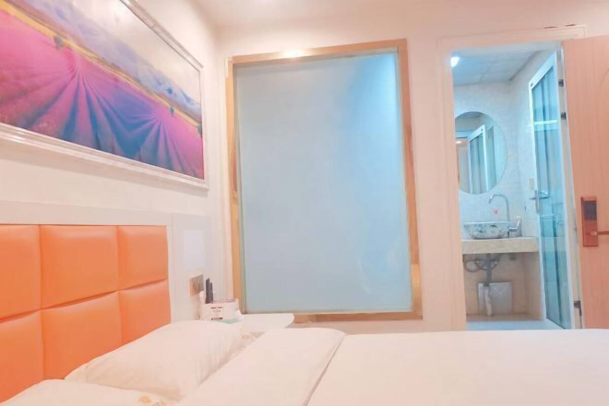 Habitación de hotel con cama, un cuadro grande, baño visible a través de una puerta abierta y cabecero de madera.