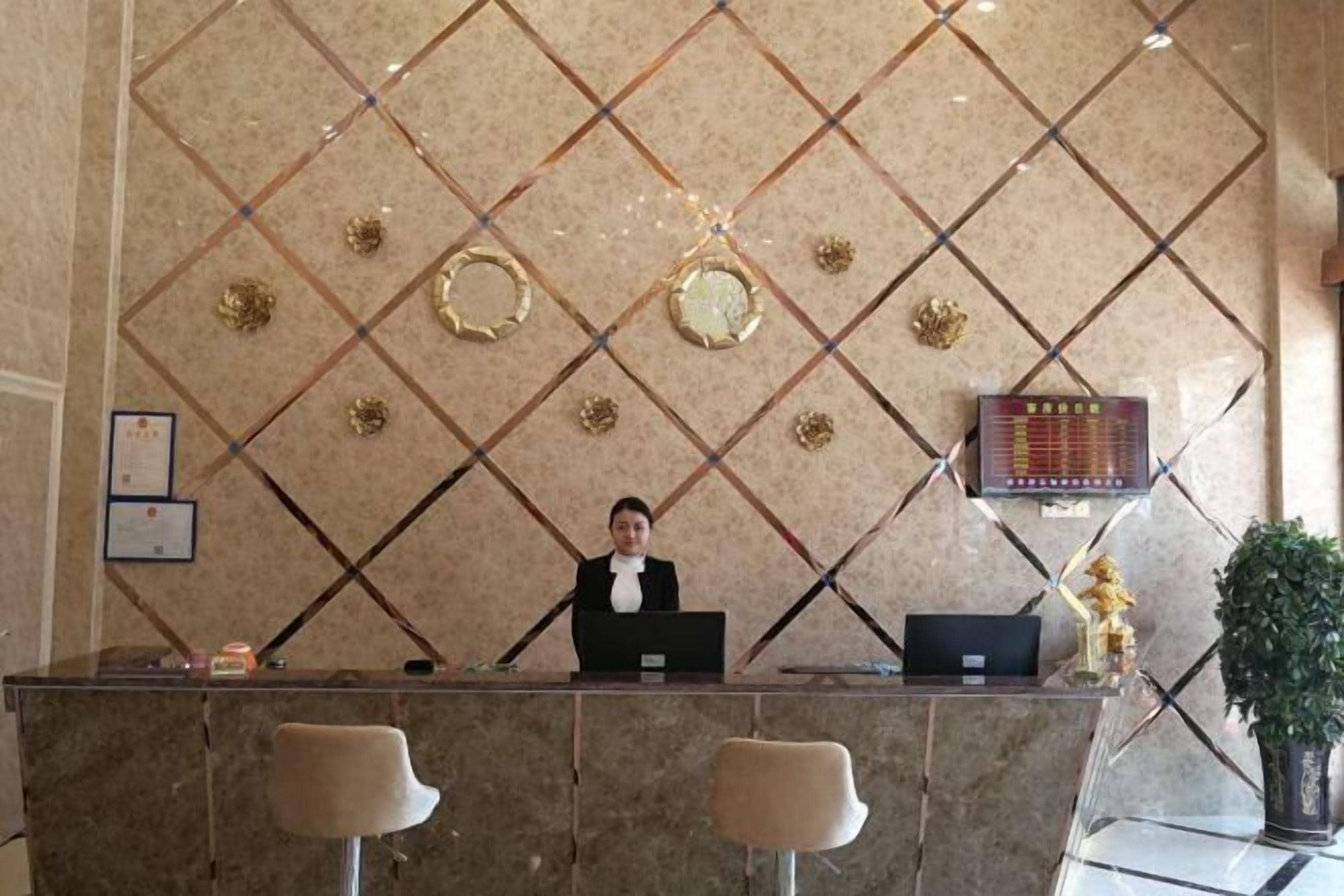 Un comptoir d’accueil avec un réceptionniste, un écran numérique et un mur décoratif orné de motifs géométriques.