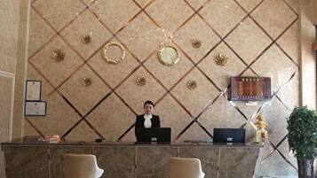 Un comptoir d’accueil avec un réceptionniste, un écran numérique et un mur décoratif orné de motifs géométriques.