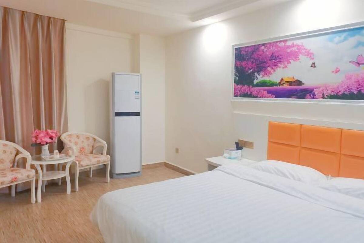 Habitación de hotel con cama, una silla, una mesa, un refrigerador y un cuadro en la pared.