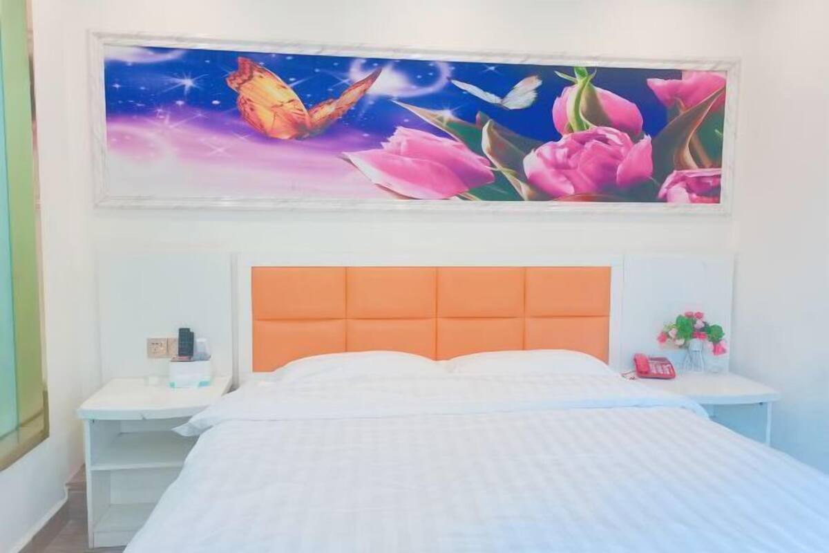 Un dormitorio con cama, mesita de noche, cabecera y una obra de arte colgada en la pared.
