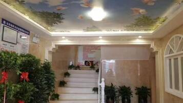 A hotel lobby with a staircase, potted plants, and a ceiling with floral decorations.