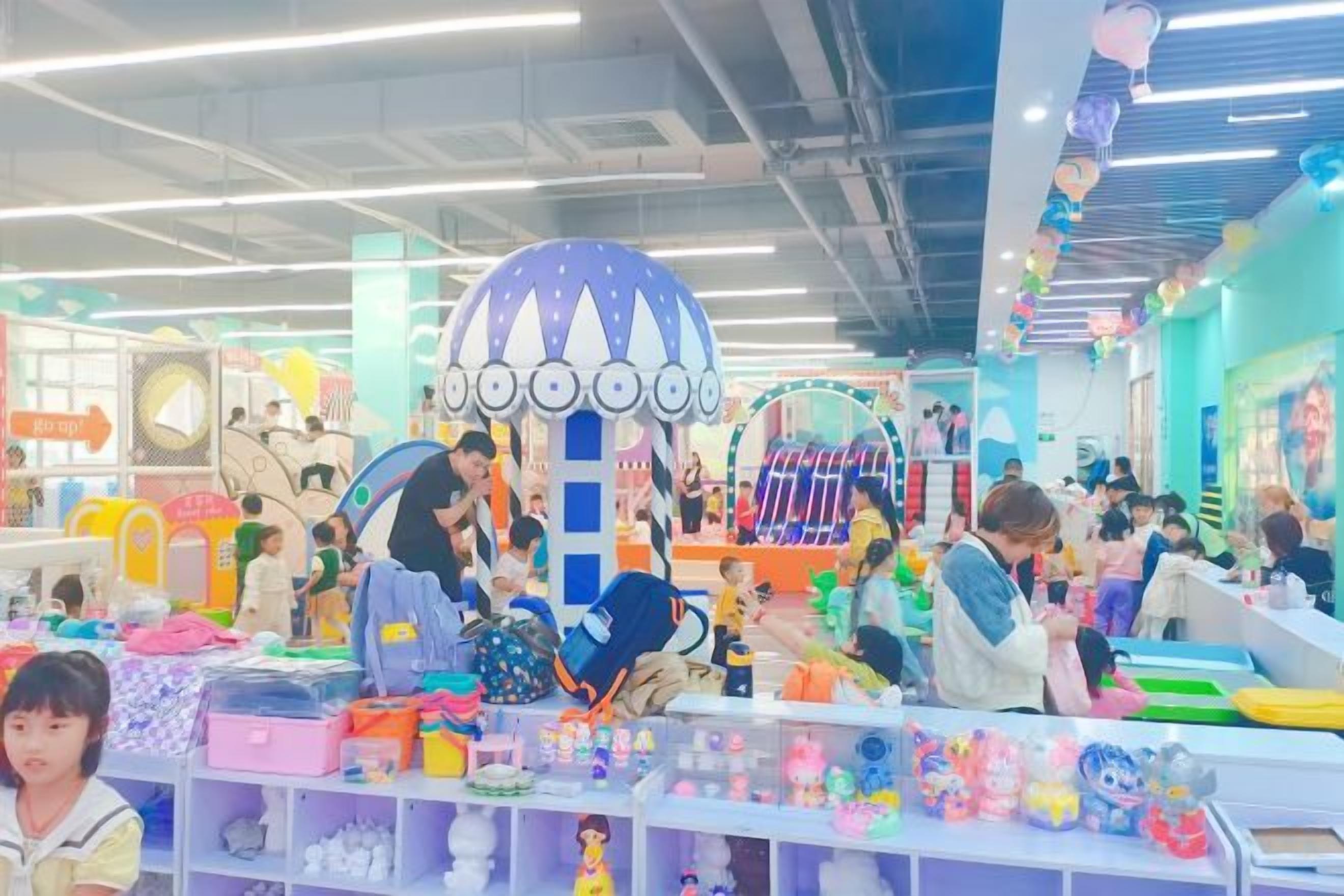 A brightly lit indoor space with various play areas and activity stations, including a large dome structure and multiple shelves with toys and games.