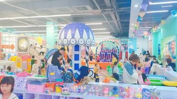 A brightly lit indoor space with various play areas and activity stations, including a large dome structure and multiple shelves with toys and games.