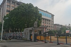 Una entrada con portón y un edificio al fondo, un árbol y motocicletas estacionadas.