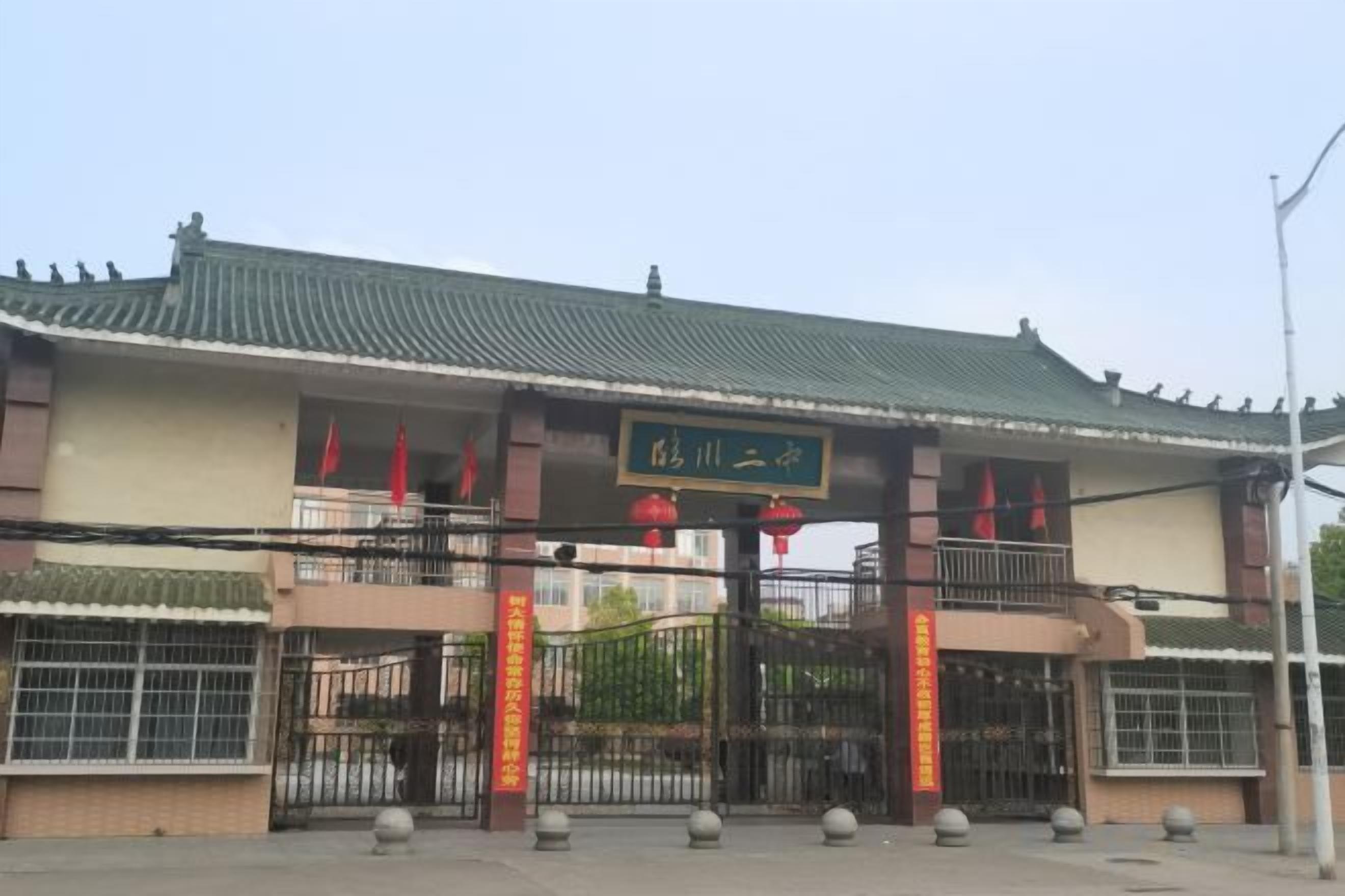 A traditional Chinese gate with a sign above it, a gated entrance with a fence, and a clear sky.