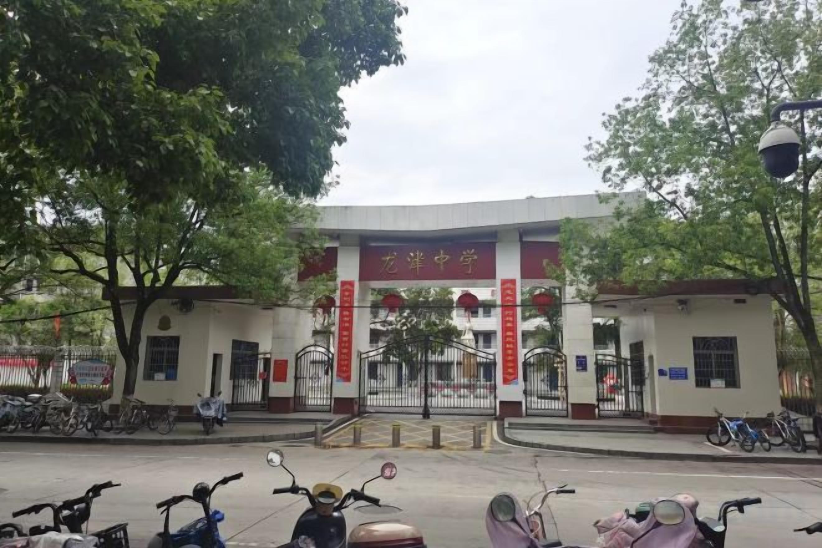 A building entrance with a red and white sign, a gated driveway, and several parked scooters.