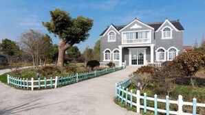 A two-story house with a grey exterior and white trim, a front porch, and a driveway leading to the entrance. - Dongping Resort (Shanghai)