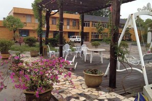 An outdoor patio area with a pergola, white plastic chairs, a table, and potted plants. - Dongping Resort (Shanghai)