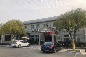 A building with a covered entrance, a parking area with cars, and trees. - Dongping Resort (Shanghai)