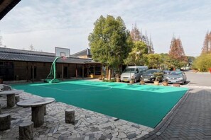 An outdoor basketball court with a green surface, surrounded by trees and parked cars. - Dongping Resort (Shanghai)