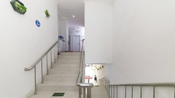A staircase with metal railings and a green directional sign at the bottom. - Chunxin Hostel (Shanghai)