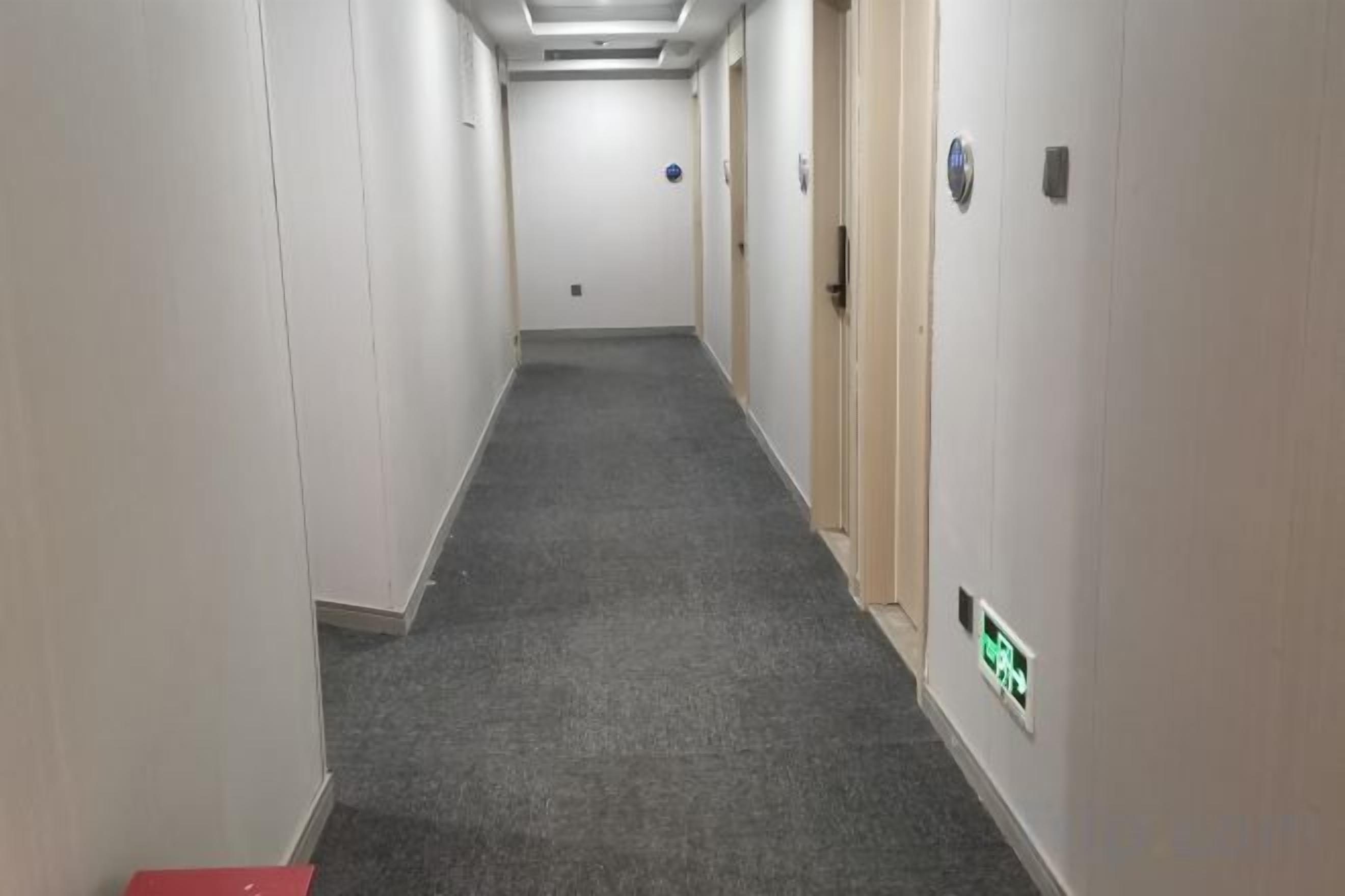 A narrow hallway with carpeted floors and white walls, leading to a door at the end.