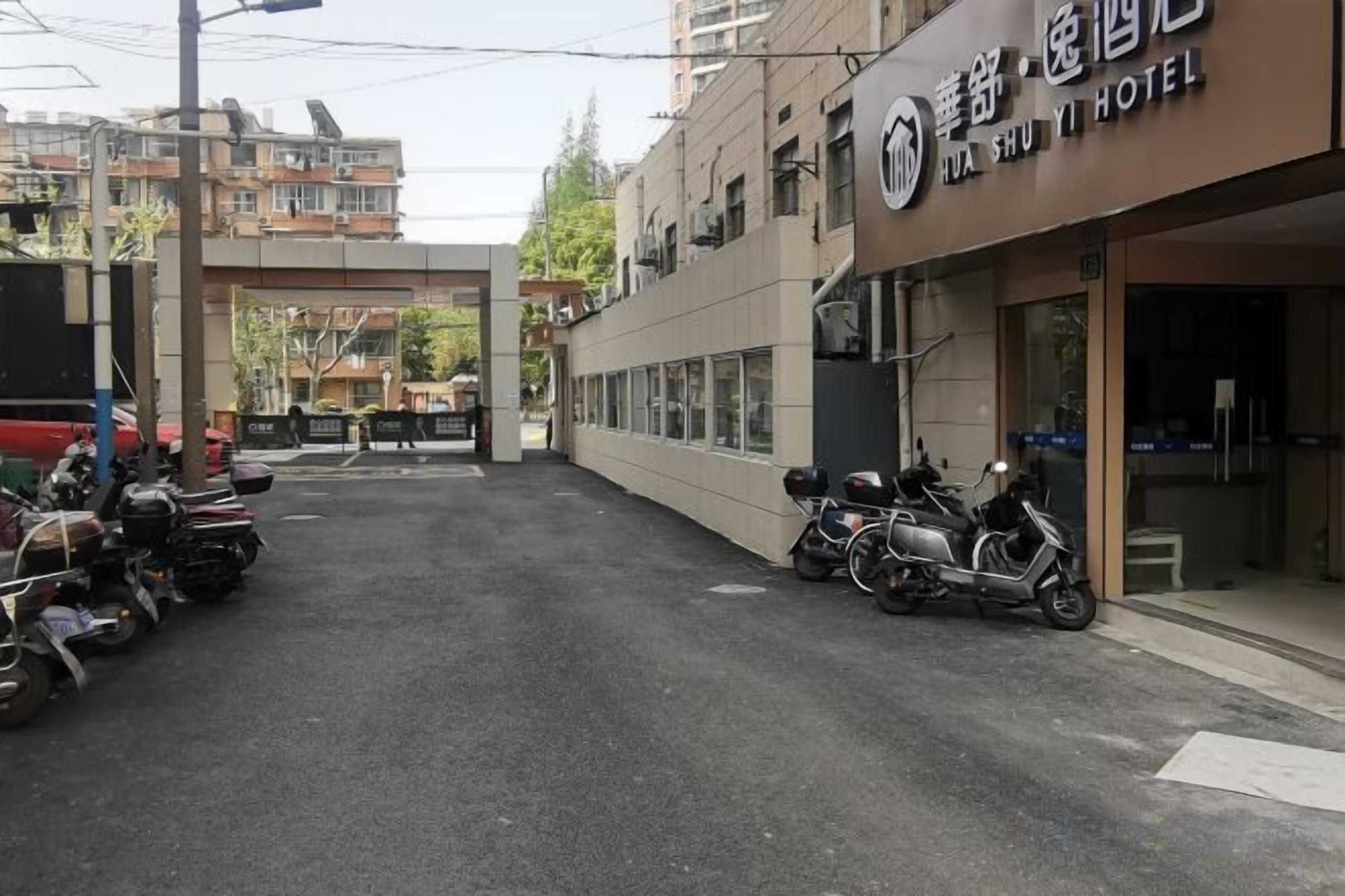 Entrada de hotel com galeria coberta, motocicletas estacionadas e um edifício com letreiros.