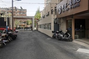 A hotel entrance with a covered walkway, parked motorcycles, and a building with signage. - Huashuyi Hostel (Shanghai Kongjiang Road) (Shanghai)