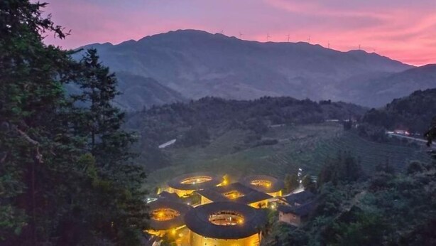 Un complejo de edificios circulares con varias estructuras, rodeado de terreno montañoso y un cielo al atardecer.