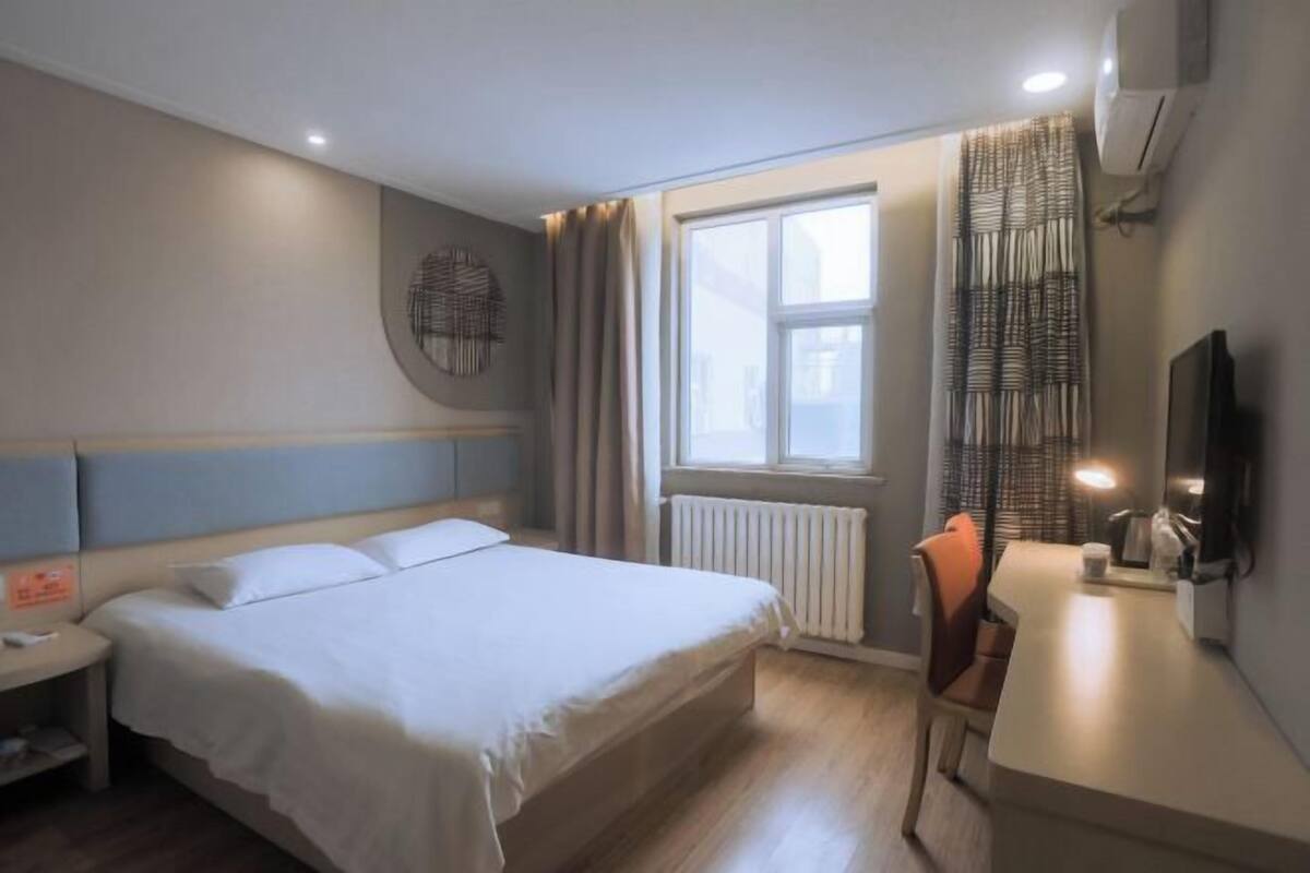 A hotel room with a bed, bedside table, chair, desk, and a television.